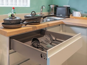 A kitchen with a wooden countertop, a stove, a sink, and a drawer with kitchen utensils.