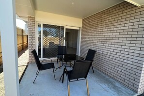 A patio with a table and chairs, a sliding glass door, and a brick wall.