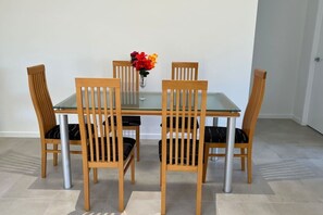 A dining table with four wooden chairs, a glass top, and a vase with flowers.