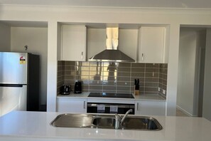 A compact kitchen with white cabinetry, a stainless steel range hood, a built-in dishwasher, and a sink with a modern faucet.