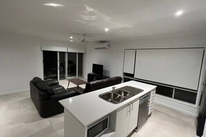 A modern kitchen with a central island, a dining area with a sofa, and a large window. - New house(Master with ensuite and A/C)2 Bath (Flagstone)