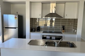 A modern kitchen with a stainless steel refrigerator, a built-in stove, and a large range hood.