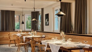 Un comedor con mesas y sillas de madera, manteles blancos y lámparas colgantes.