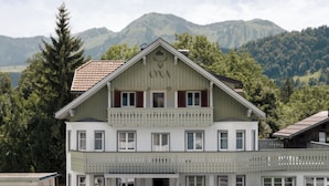 Un edificio de dos pisos con balcón y montañas al fondo.