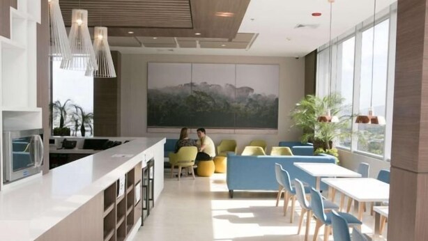 Une cuisine moderne dotée d'un îlot central, d'un coin repas avec des chaises bleues et des canapés jaunes, et de grandes fenêtres qui laissent entrer la lumière naturelle.
