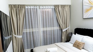 A neatly made bed with a white comforter and a beige pillow, a television mounted on the wall, and a window with beige curtains. - Charming 2-bedroom apartment with AC in vibrant Dubai-Jumeira Village Circle (Dubai)