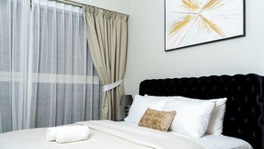 A neatly made bed with white linens and a folded towel, a black upholstered headboard, and a framed abstract art piece on the wall. - Charming 2-bedroom apartment with AC in vibrant Dubai-Jumeira Village Circle (Dubai)