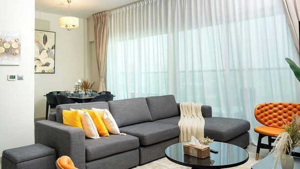 A modern living room with a grey sofa, orange chair, and a glass coffee table. - Charming 2-bedroom apartment with AC in vibrant Dubai-Jumeira Village Circle (Dubai)