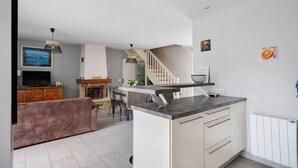 A modern kitchen with a central island, a dining area with chairs, a fireplace, and a staircase leading to another level. - House - Le Clos Des Pommiers (Pleudihen-sur-Rance)