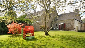 A stone building with a red door, a lawn, and a tree with pink flowers. - House - Le Clos Des Pommiers (Pleudihen-sur-Rance)