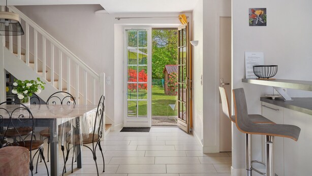 A modern kitchen with a dining area, a staircase, and a view of a garden through glass doors. - House - Le Clos Des Pommiers (Pleudihen-sur-Rance)