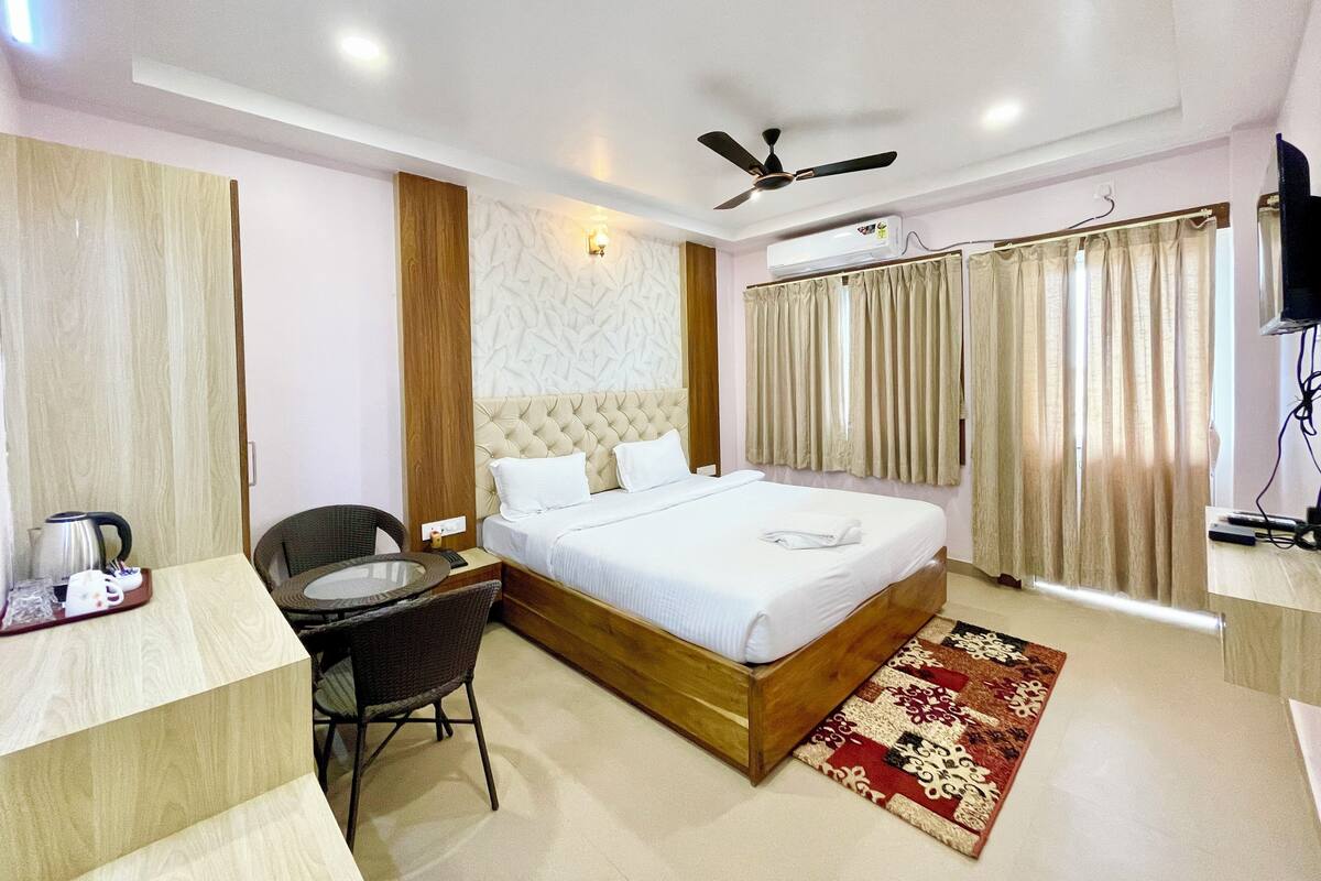 Una habitación de hotel con una cama, un escritorio con una silla, un ventilador de techo y un televisor.