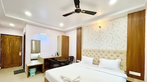 A hotel room with a bed, a desk, a chair, a ceiling fan, and a wall with a leaf pattern. - New Beach Resort - near Sea Beach (Brahmagiri)