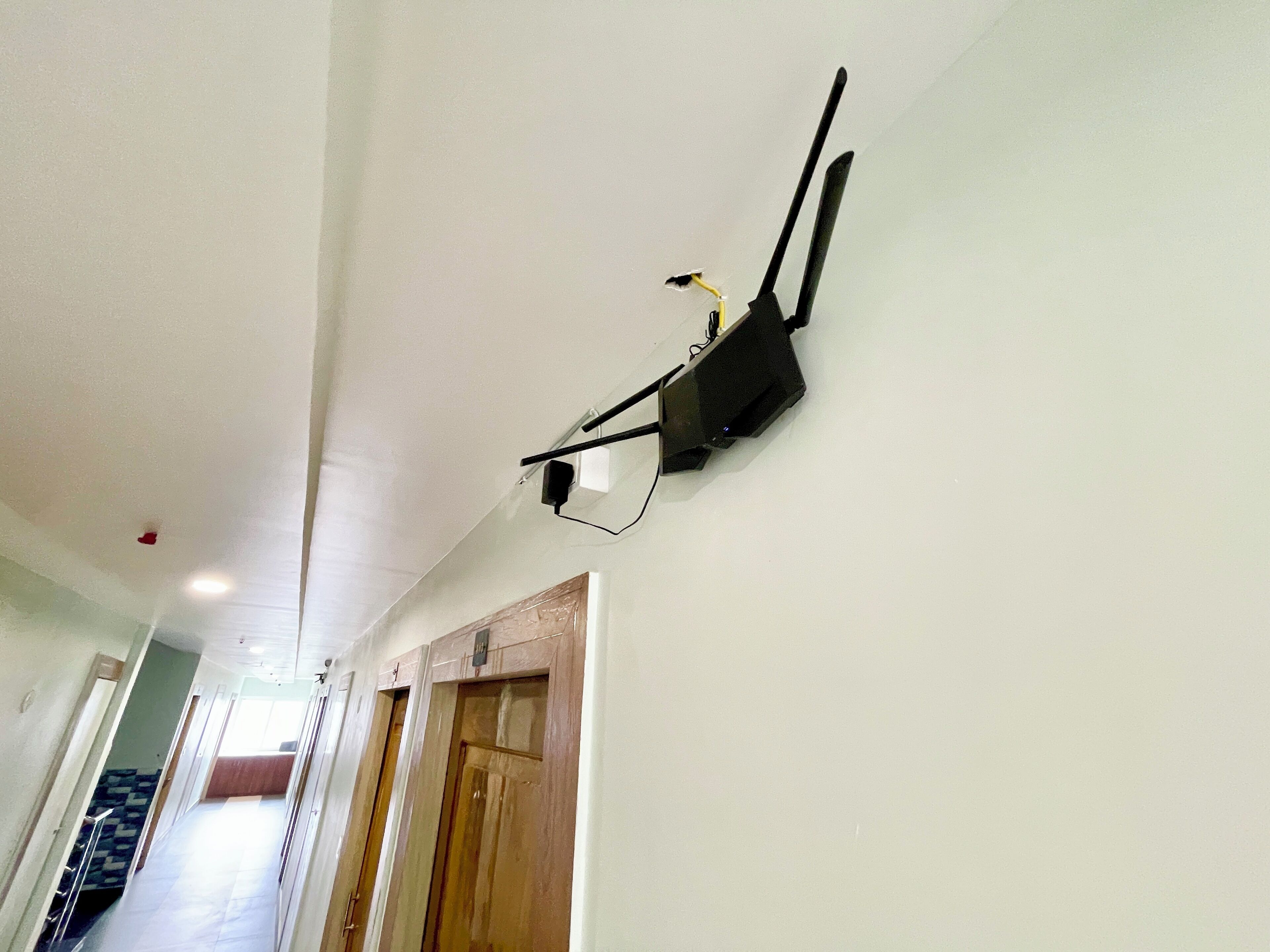 A hallway with white walls, a ceiling-mounted security camera, and wooden doors.