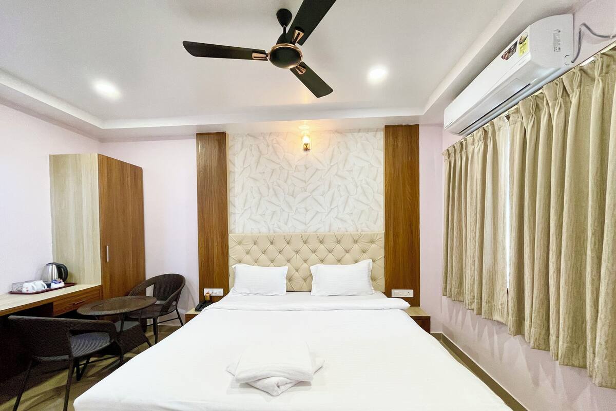 Habitación de hotel con cama, escritorio, silla, ventilador de techo y aire acondicionado instalado en la pared.