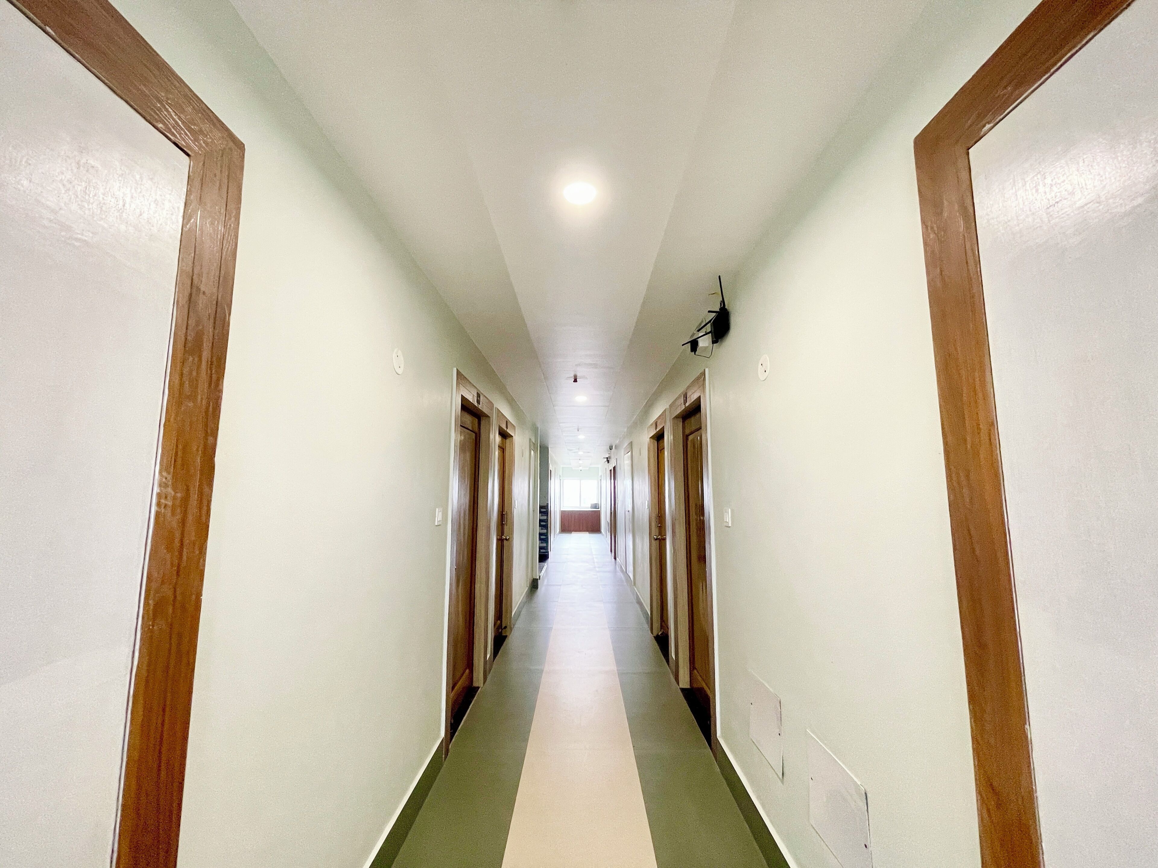 A long, narrow hallway with wooden doors on both sides, leading to individual rooms.