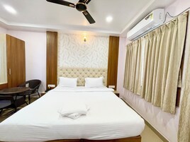 Une chambre d’hôtel avec un grand lit, un ventilateur de plafond, un appareil de climatisation, une lampe fixée au mur et une fenêtre avec des rideaux.