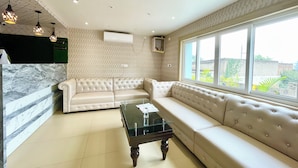 A modern living room with a beige sofa, a glass coffee table, and pendant lighting. - New Beach Resort - near Sea Beach (Brahmagiri)