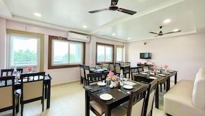A dining area with multiple tables and chairs, ceiling fans, and a television on the wall. - New Beach Resort - near Sea Beach (Brahmagiri)
