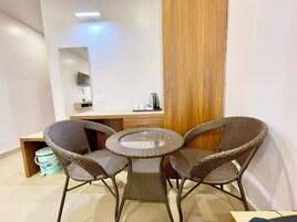 Una habitación pequeña y moderna con una mesa redonda de vidrio, sillas de mimbre, un armario de madera y un espejo grande.