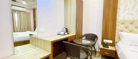 A hotel room with a bed, a desk with a chair, a small table, a mirror, and a wardrobe.