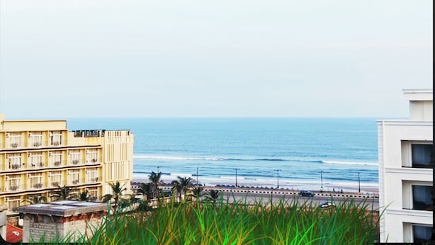 A coastal view with a beachfront promenade, a multi-story building with balconies, and a clear view of the ocean. - New Beach Resort - near Sea Beach (Brahmagiri)
