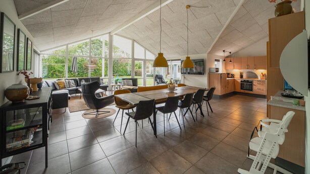 Een ruime keuken met moderne apparatuur, een eethoek met een grote tafel en stoelen, en uitzicht op groen door grote ramen.