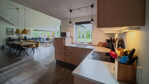 Een moderne keuken met een groot eiland, veel natuurlijk licht en een eethoek met uitzicht.