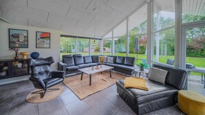 Een moderne woonkamer met een hoekbank, een salontafel en een eettafel. Grote ramen bieden uitzicht op het omliggende landschap.