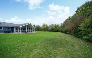 A house with a covered patio, a lawn, and a wooded area.
