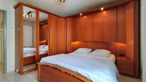 A bedroom with a large bed, wooden wardrobe, and a mirror. - 2 bedroom lovely apartment in Oostende (Oostende)