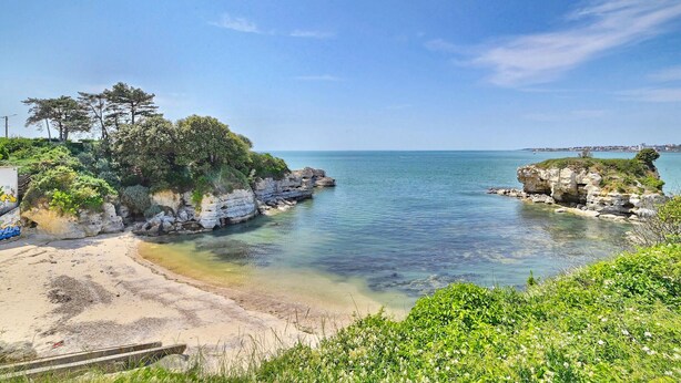 A coastal landscape with clear waters, rocky outcrops, and a sandy beach.