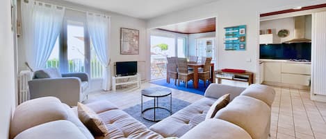 A living room with a sofa, TV, and dining area with chairs and a table.