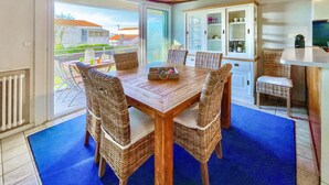 A dining area with a wooden table and wicker chairs, a cabinet with glass doors, and a view of the outside.