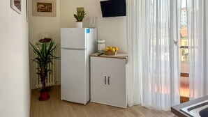 Una cucina compatta con un frigorifero, un piccolo armadietto, una pianta in vaso e un cesto di frutta sul piano di lavoro.