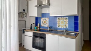 Una cucina compatta con mobili bianchi, un lavello in acciaio inossidabile e vivaci piastrelle decorative blu.
