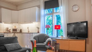 Una sala de estar moderna con sofá, mesa de centro, televisor y un área de cocina con alacenas blancas y microondas.