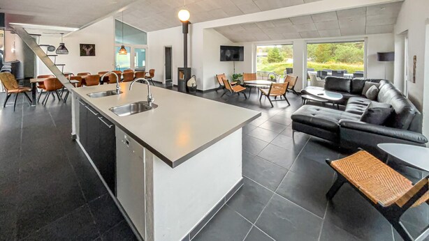 A modern kitchen with a central island, a dining area with chairs, and a living area with a sofa and a coffee table. - Nice home in Blåvand with sauna (Blåvand)
