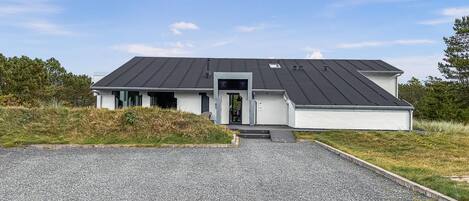 A modern two-story house with a dark roof, a front entrance, and a gravel driveway.