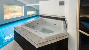 A spa area with a large hot tub, a small window, and a view of a pool. - Nice home in Blåvand with sauna (Blåvand)