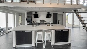 A modern kitchen with a large island, black cabinets, white stools, and a stainless steel sink. - Nice home in Blåvand with sauna (Blåvand)