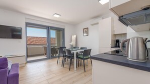 A modern apartment with a balcony, a dining area, a kitchenette, and a flat-screen TV.
