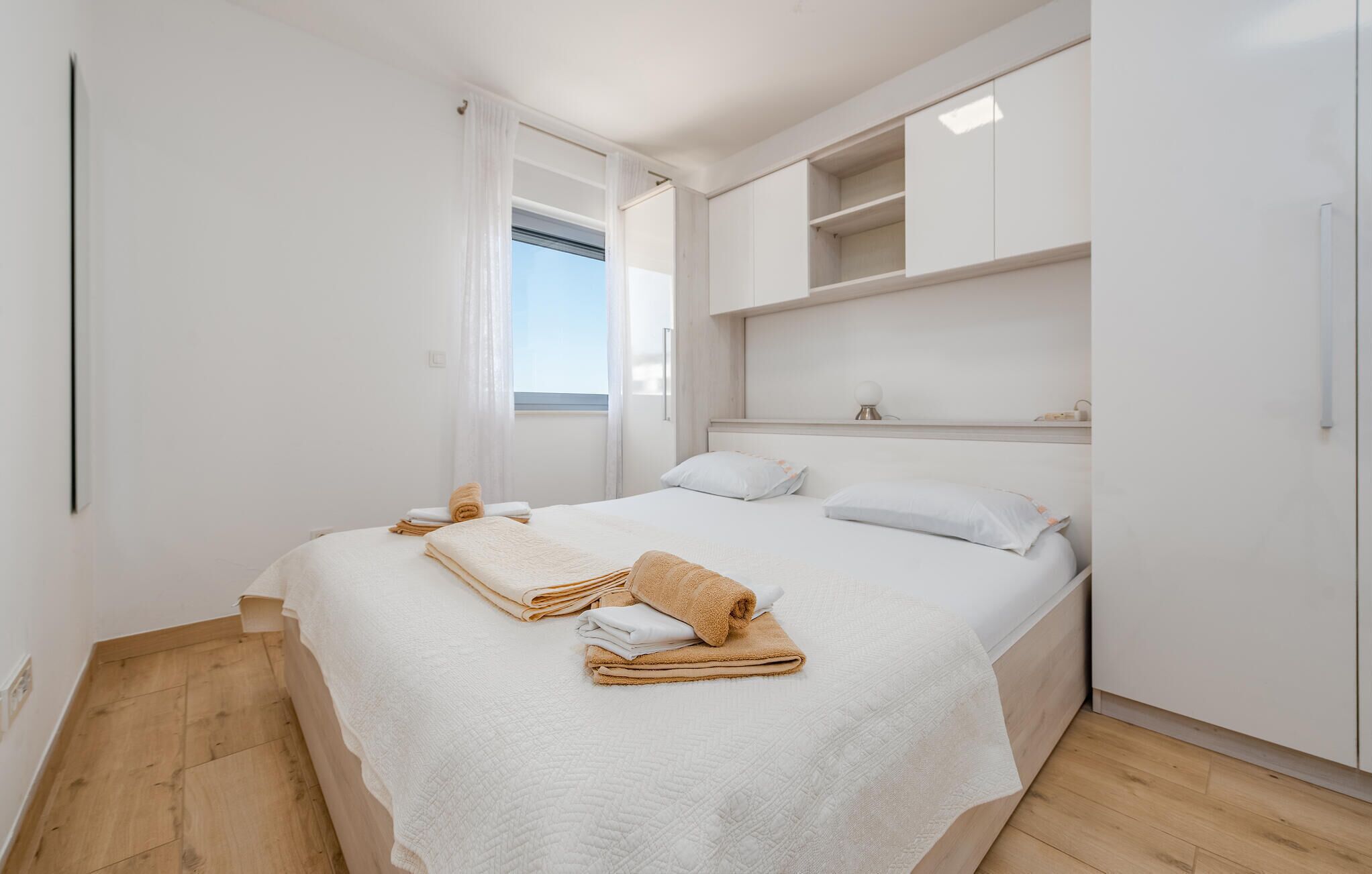 A bedroom with a bed, a window, and built-in storage cabinets.