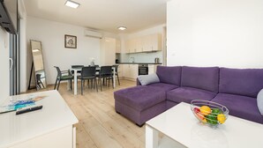 A modern living room with a purple sofa, a dining table with chairs, and a kitchen area with cabinets and appliances.