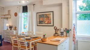 Een gezellige keuken met een houten tafel, stoelen, een koffiezetapparaat en een raam met uitzicht op groen.