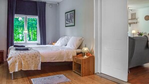 Een slaapkamer met een bed, nachtkastje, lamp en uitzicht op groen buiten het raam.
