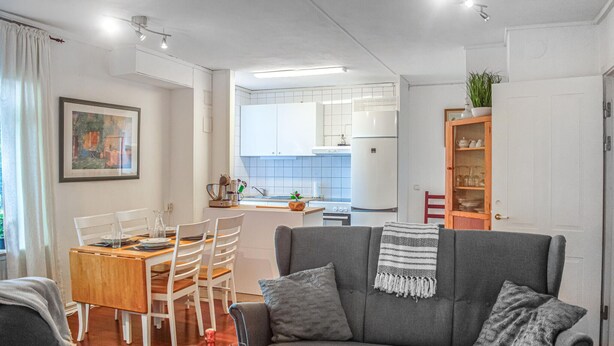 Een moderne woonkamer met een grijze bank, een eettafel met stoelen, en een keuken op de achtergrond.