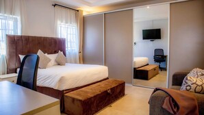 Habitación de hotel moderna con una cama grande, un escritorio, una silla, un sofá, un televisor y un armario con puerta corredera.