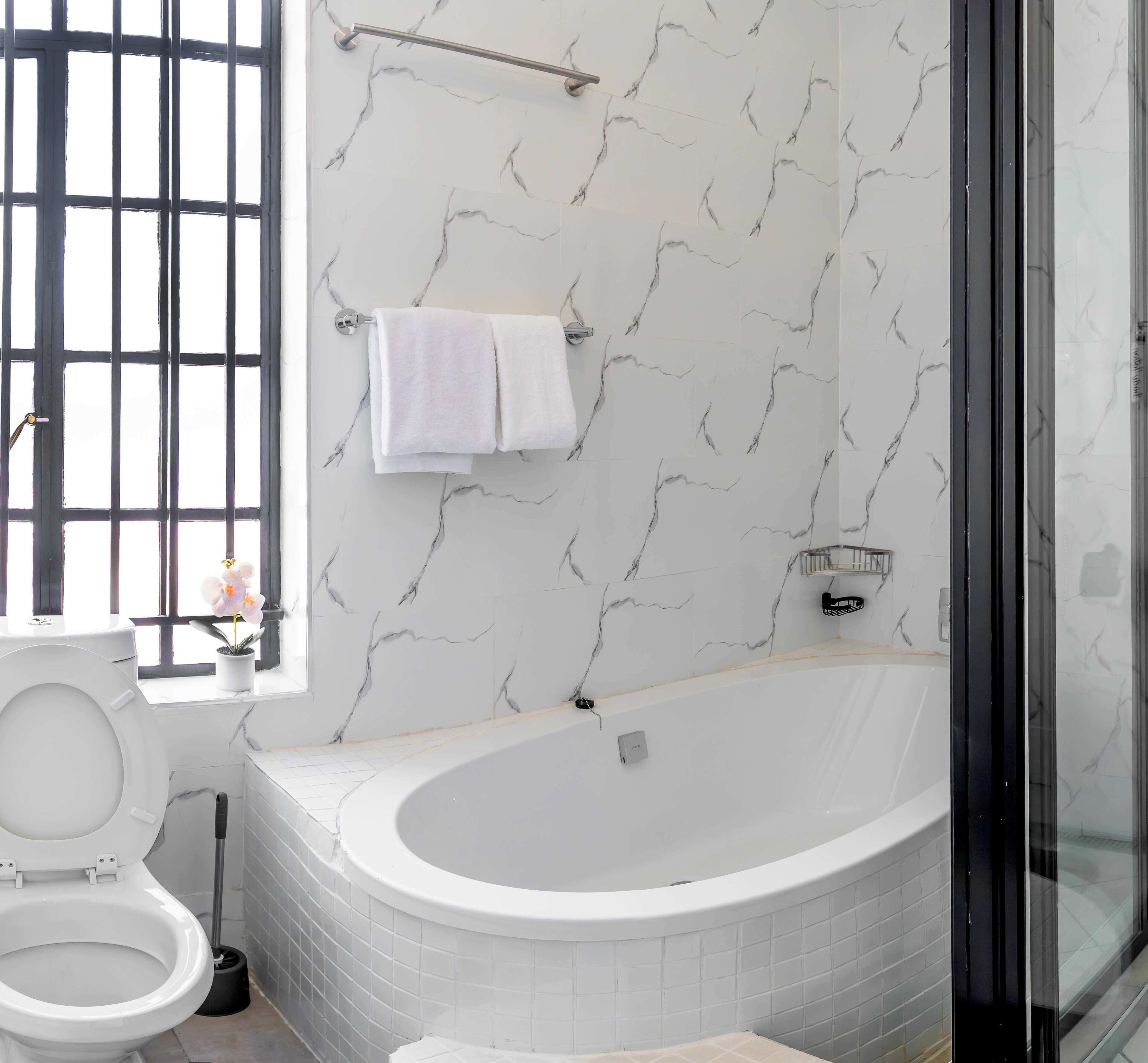 Un baño con inodoro, bañera y una ventana con barrotes.