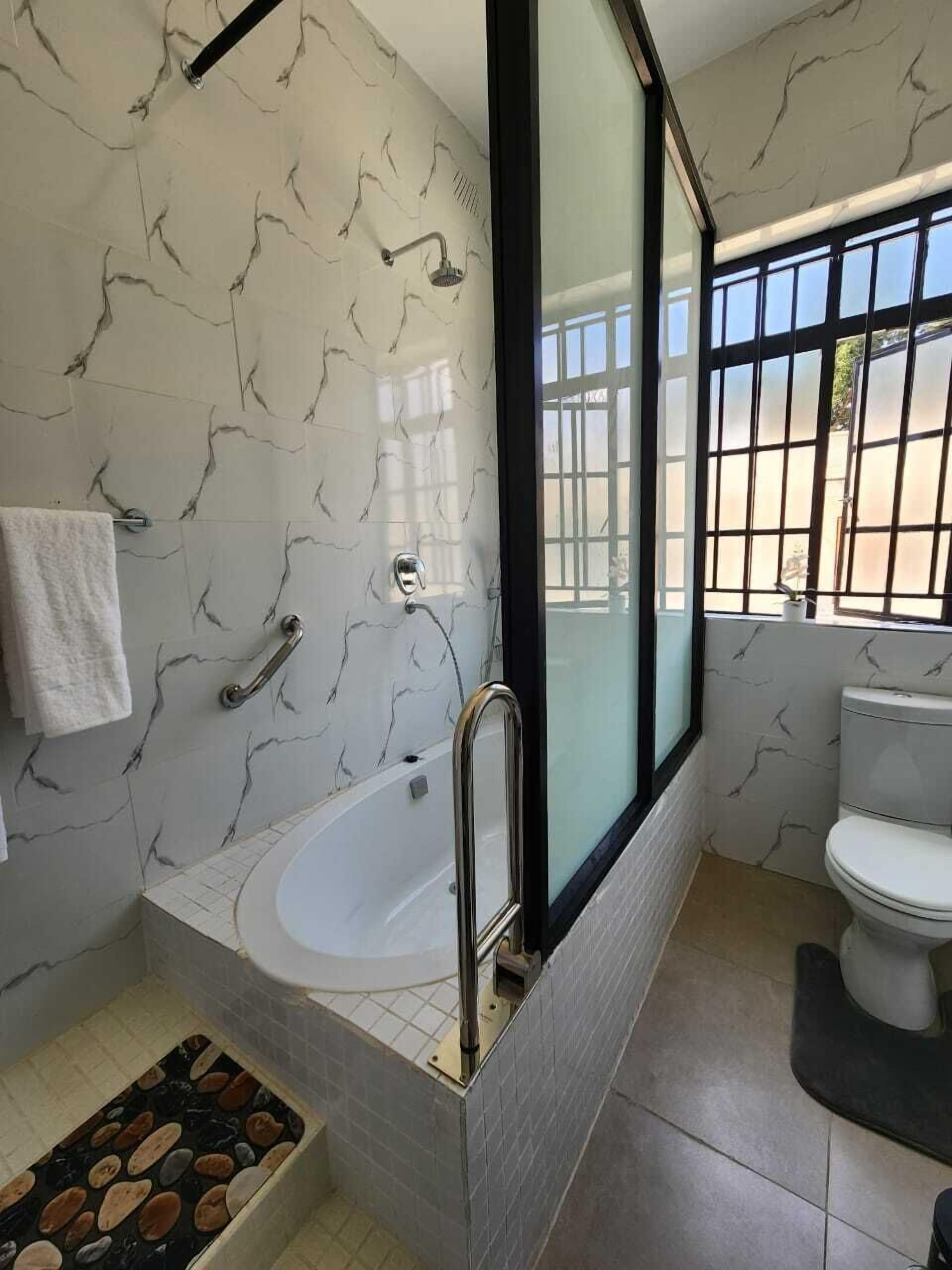 Une salle de bain avec une baignoire, des toilettes et une fenêtre avec des barreaux.